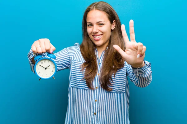 Mujer joven con despertador contra fondo azul — Foto de Stock