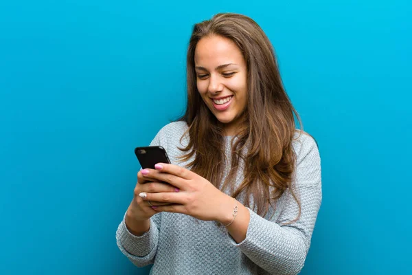 Ung kvinna med mobiltelefon mot blå bakgrund — Stockfoto