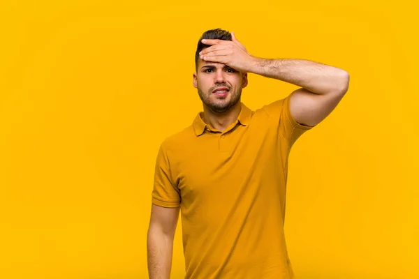 young hispanic man panicking over a forgotten deadline, feeling stressed, having to cover up a mess or mistake against orange wall