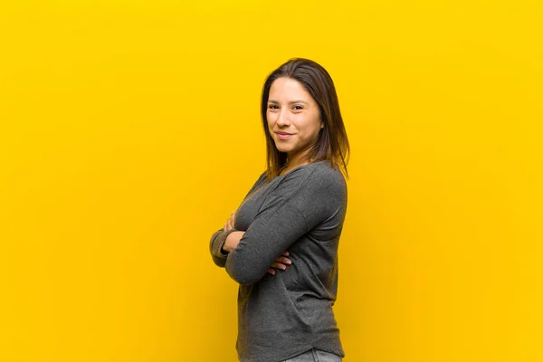 latin american woman smiling to camera with crossed arms and a happy, confident, satisfied expression, lateral view isolated against yellow wall