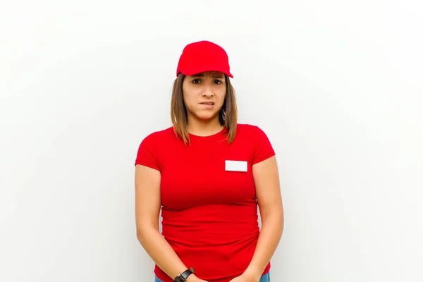 delivery woman looking puzzled and confused, biting lip with a nervous gesture, not knowing the answer to the problem against white background