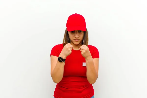 delivery woman looking confident, angry, strong and aggressive, with fists ready to fight in boxing position against white background