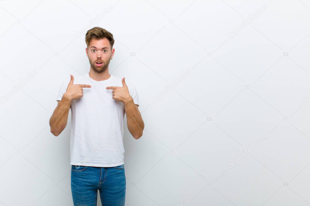 young man feeling happy, surprised and proud, pointing to self with an excited, amazed look against white background