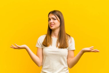 Genç, güzel bir kadın şaşkın, kafası karışmış ve stresli görünüyor, farklı seçenekler arasında merak ediyor, turuncu arka planda belirsizlik hissediyor.