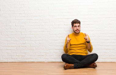 Genç yakışıklı adam tuğla duvar dokusuna karşı evde oturuyor.