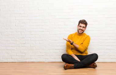 Genç yakışıklı adam tuğla duvar dokusuna karşı evde oturuyor.