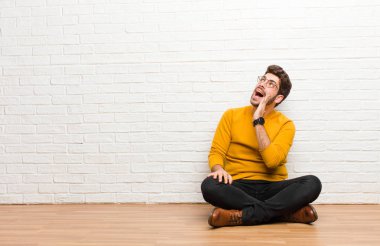 Genç yakışıklı adam tuğla duvar dokusuna karşı evde oturuyor.