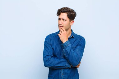 Şaşırmış, gergin, endişeli ya da korkmuş bakışları olan genç yakışıklı bir adam mavi arkaplana karşı fotokopi alanına bakıyor.