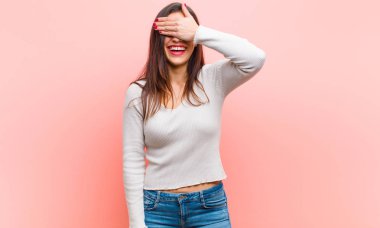 Genç ve güzel bir kadın tek eliyle gözlerini kapatıyor. Korkmuş ya da endişeli hissediyor, merak ediyor ya da körü körüne pembe arka plana karşı bir sürpriz bekliyor..