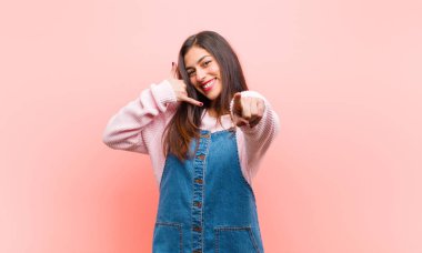 Genç, güzel bir kadın neşeyle gülümsüyor ve kamerayı işaret ediyor. Daha sonra seni arayıp pembe arka planda telefonla konuşuyor..