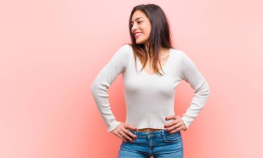 Genç, güzel bir kadın mutlu, neşeli ve kendinden emin görünüyor. Gururla gülümsüyor ve pembe arka planda iki elinle kalçanın yanında yer almak istiyor..