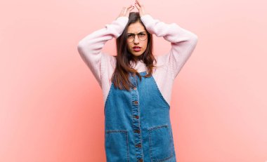 Genç ve güzel bir kadın stresli ve endişeli, depresif ve hayal kırıklığına uğramış hissediyor, iki elini de pembe arka plana doğru kaldırıyor..