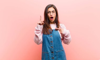 Genç ve güzel bir kadın gururlu ve şaşırmış hissediyor, özgüvenini gösteriyor, pembe arka planda bir numara gibi hissediyor..