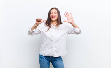 Genç, güzel bir kadın gülümsüyor ve arkadaş canlısı görünüyor. Altı ya da altıncı numarayı gösteriyor. Eli önde, beyaz duvara karşı geriye doğru sayıyor.