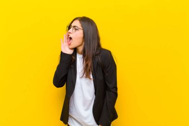 Genç ve güzel bir kadın profili, mutlu ve heyecanlı görünüyor, bağırıyor ve turuncu duvara karşı alanı kopyalamak için çağırıyor.