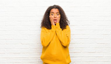 Genç siyahi kadın şok olmuş ve korkmuş hissediyor. Ağzı açık ve elleri tuğla duvarda.