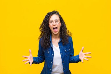 Genç, güzel bir kadın kendini mutlu, şaşkın, şanslı ve şaşırmış hissediyor. Turuncu duvara karşı inanılmaz.