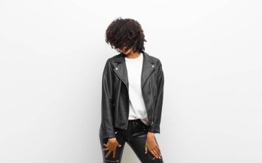 Genç, güzel siyah kadın beyaz duvara karşı deri ceket giyip dans ediyor.