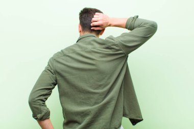 Genç yakışıklı adam düşünüyor ya da şüphe ediyor, kafasını kaşıyor, şaşkın ve kafası karışık hissediyor, arkaya ya da arkaya bakıyor.