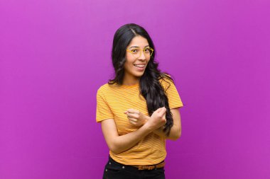 genç güzel latin kadın neşeyle gülümseyen ve kutluyor, yumruklar sıkılmış ve kollar geçti, mor duvara karşı mutlu ve olumlu duygu