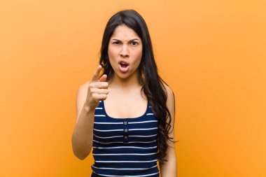 Genç, güzel İspanyol bir kadın, kızgın agresif bir ifadeyle kameraya bakıyor. Kahverengi duvara karşı öfkeli, çılgın bir patron gibi görünüyor.