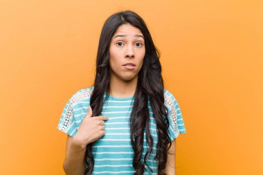 Genç, güzel, İspanyol bir kadın kafası karışık, şaşkın ve güvensiz hissediyor. Kendini merak edip bana mı soruyor? kahverengi duvara yaslan