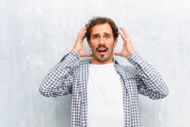 Genç yakışıklı adam ellerini havaya kaldırarak bağırıyor. Öfkeli, sinirli ve üzgün hissediyor. Duvara yaslanmış.