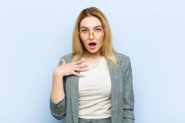Genç, güzel sarışın kadın şok olmuş, şaşırmış ve şaşırmış hissediyor, elleri göğsünde ve ağzı açık, kim diyor, ben mi? yassı duvara karşı