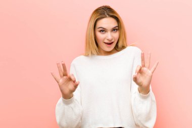 Genç, güzel sarışın kadın şok olmuş, şaşırmış ve şaşırmış hissediyor. Onaylıyor. İki eliyle pembe düz duvara işaret veriyor.