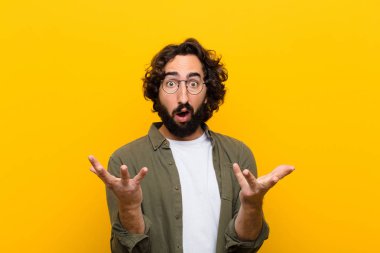 Genç çılgın adam son derece şok olmuş ve şaşırmış, endişeli ve paniklemiş hissediyor, sarı duvara karşı stresli ve dehşete düşmüş bir bakışla