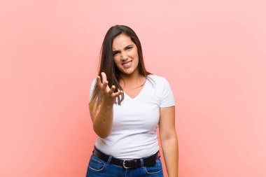 Genç, güzel, İspanyol bir kadın kızgın, sinirli ve sinirli görünüyor. Pembe duvara karşı senin neyin var? 