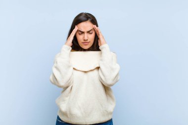 Genç ve güzel bir kadın stresli ve hayal kırıklığına uğramış görünüyor. Baskı altında çalışıyor ve mavi arka planda sorunlar yaşıyor.