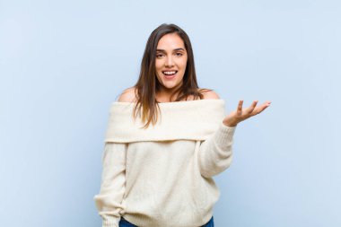 Genç, güzel bir kadın kendini mutlu, şaşırmış ve neşeli hissediyor. Pozitif bir tavırla gülümsüyor. Mavi arka plana karşı bir çözüm ya da fikir buluyor.