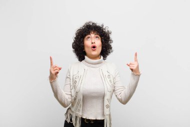 Genç, güzel afro kadın şaşırmış, şaşkın ve ağzı açık görünüyor, iki eliyle uzayı kopyalamak için yukarı bakıyor.