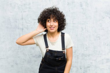 Genç, güzel afro kadın gülümsüyor, tuhaf bir şekilde yan tarafa bakıyor, dedikoduları dinlemeye ya da bir sırrı duymaya çalışıyor.