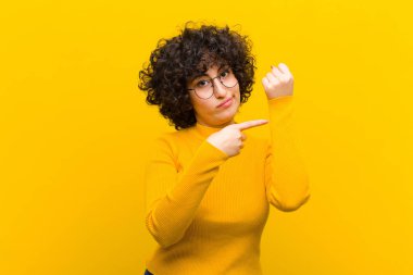 Genç ve güzel afro kadın sabırsız ve kızgın görünüyor, saati gösteriyor, dakiklik istiyor, zamanında gelmek istiyor.