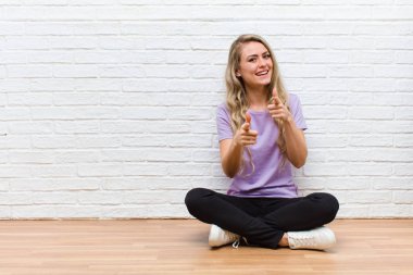 Genç, sarışın, güzel bir kadın. Pozitif, başarılı, mutlu bir tavırla gülümsüyor. Kamerayı işaret ediyor, elleriyle silah işareti yapıyor.