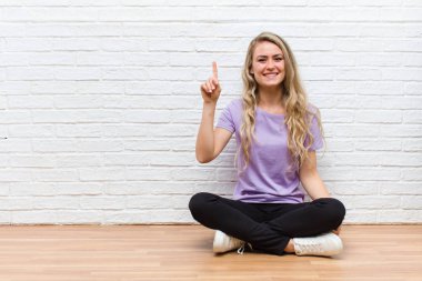 Genç sarışın güzel kadın mutlu ve mutlu bir şekilde gülümsüyor, tek eliyle boşluğu dolduruyor.