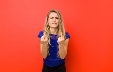 Genç sarışın kadın kışkırtıcı, agresif ve müstehcen hissediyor. Kırmızı duvara karşı isyankar bir tavırla orta parmağını hareket ettiriyor.