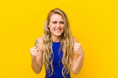 Genç sarışın kadın şok olmuş, heyecanlı ve mutlu, gülüyor ve başarıyı kutluyor, vay canına! sarı duvara yaslan