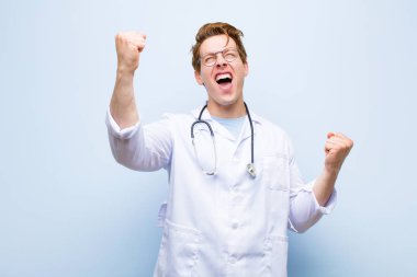 Genç kızıl saçlı doktor zafer çığlıkları atıyor. Heyecanlı, mutlu ve şaşırmış görünüyor. Mavi duvara karşı kutlama yapıyor.
