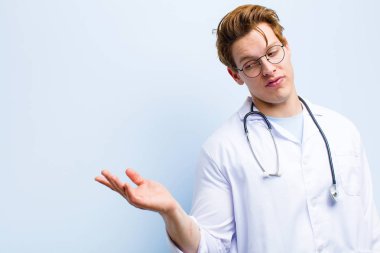 Genç kızıl saçlı doktor mutlu ve gülümsüyor. Mavi duvara karşı elinde tuttuğu bir nesneye ya da konsepte bakıyor.