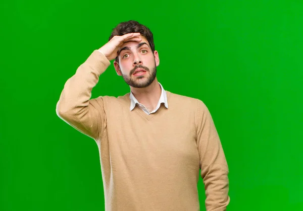 young businessman panicking over a forgotten deadline, feeling stressed, having to cover up a mess or mistake against green background