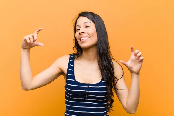 young pretty hispanic woman framing or outlining own smile with both hands, looking positive and happy, wellness concept against brown wall