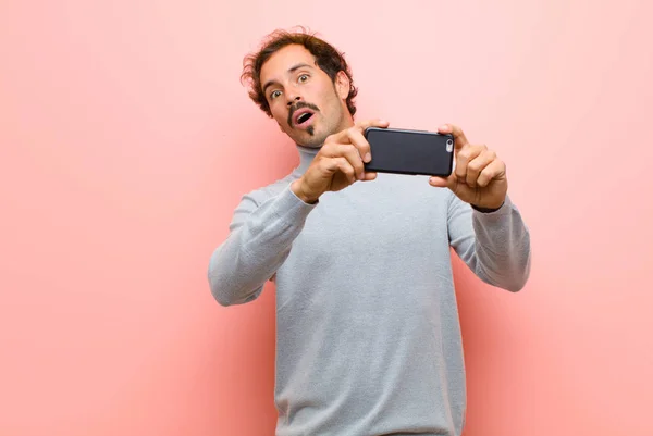 年轻英俊男子 手持智能手机 靠着粉红的平板墙 — 图库照片