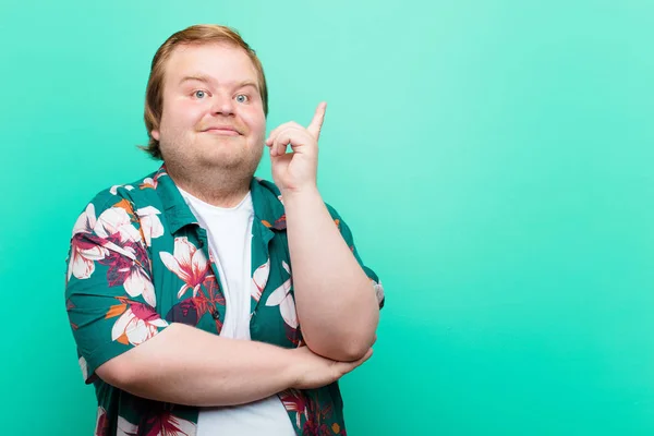 young big size man smiling happily and looking sideways, wondering, thinking or having an idea against blue wall