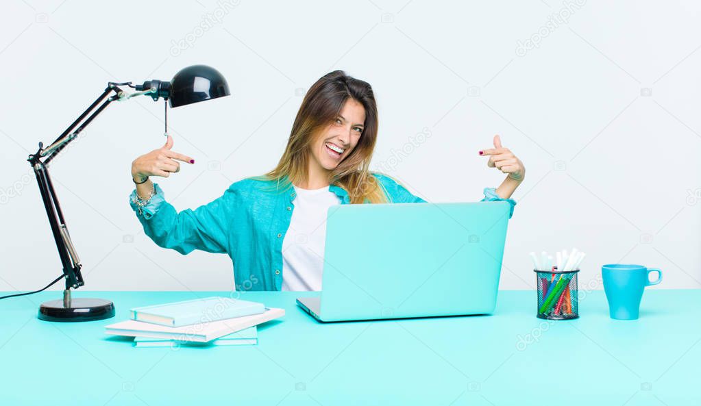 young pretty woman working with a laptop looking proud, arrogant, happy, surprised and satisfied, pointing to self, feeling like a winner