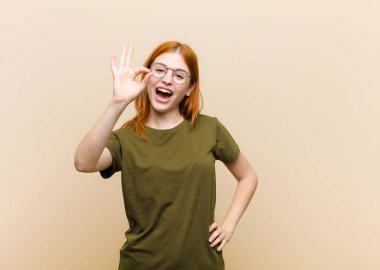 Genç kızıl saçlı güzel bir kadın kendini başarılı ve tatmin olmuş hissediyor, ağzı açık gülümsüyor, elle işaret veriyor.