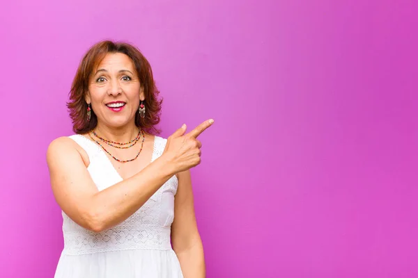 middle age woman looking arrogant, successful, positive and proud, pointing to self against purple wall