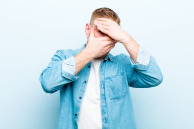 Genç kızıl saçlı adam kameraya hayır diyen iki eliyle yüzünü kapatıyor! Resimler reddediliyor ya da yumuşak mavi arkaplana karşı resimler yasaklanıyor